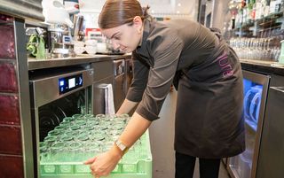 Eine junge Frau beländt einen Gastronomie-Geschirrspüler